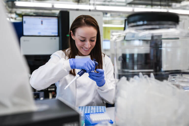 A young woman working in a sequencing lab, preparing samples, she is smiling.
