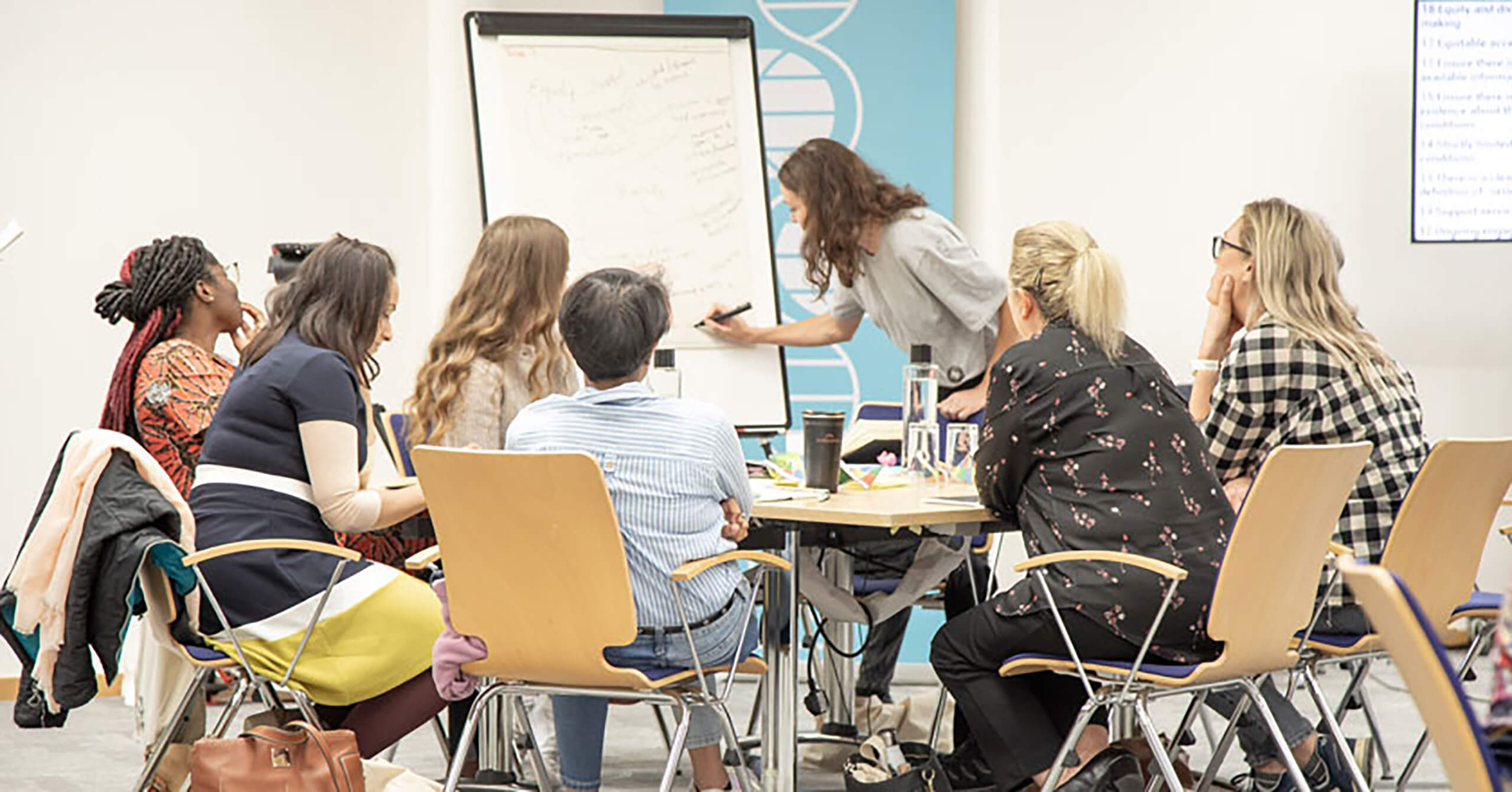 A group of people seated around a table, and one person drawing on a chart.