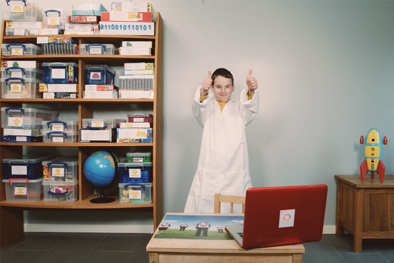 Image of little boy 'Charlie' wearing a lab coat, smiling, and giving two thumbs up