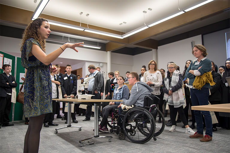 Large school group featuring teachers and pupils, including two wheelchair users, and a member of Sanger Institute faculty talking to them.