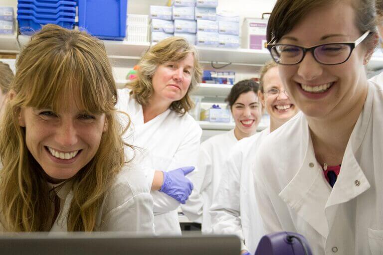 A group of teachers are in a lab, wearing lab coats and smiling.