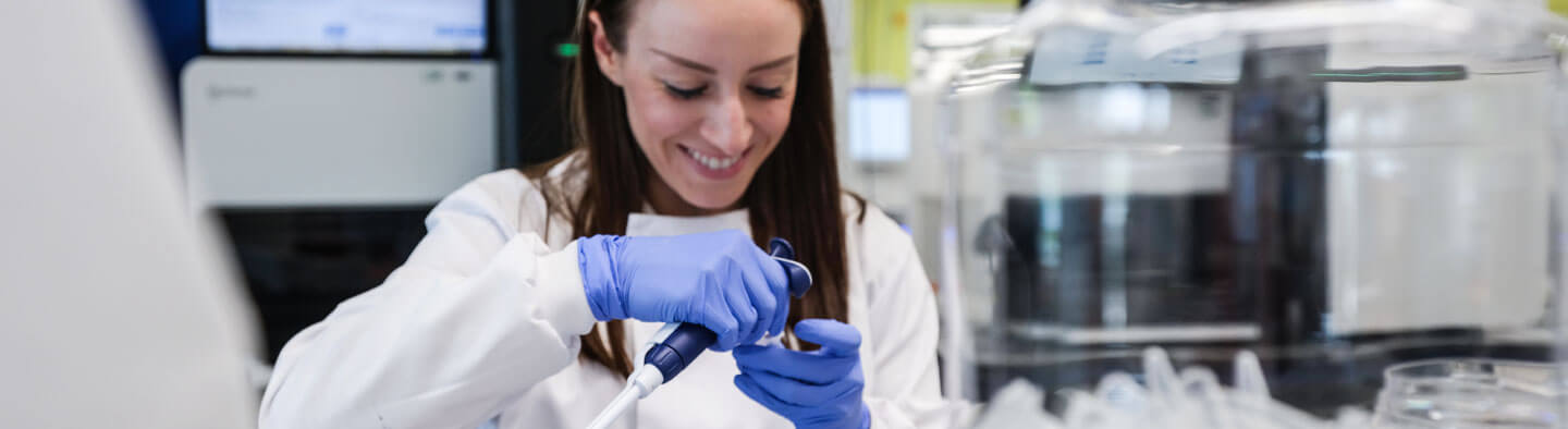 A young woman working in a sequencing lab, preparing samples, she is smiling.