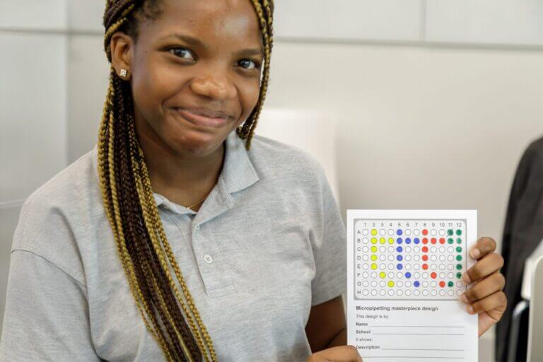 A student at the schools conference holding a micropipette activity sheet, she is smiling.