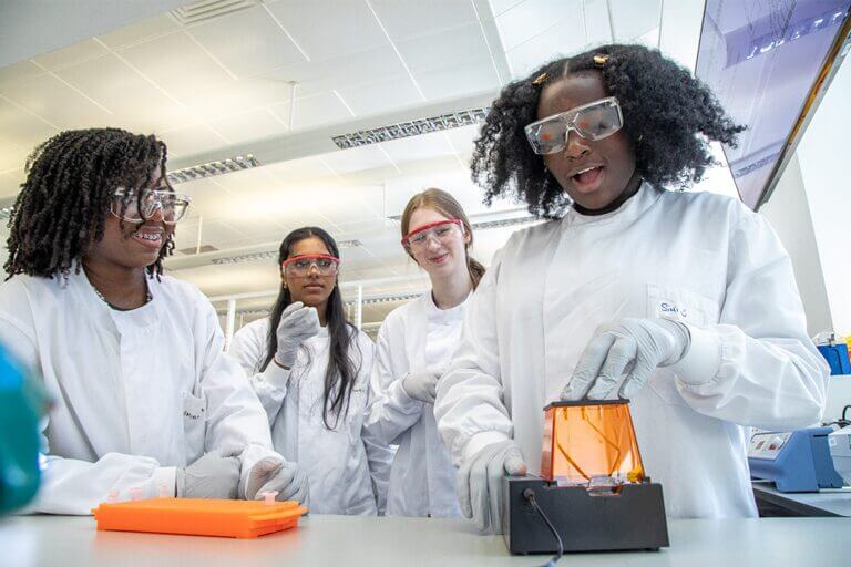 A group of young people taking part in Barcoding for Beginners, using equipment in a lab, wearing lab coats and safety goggles.